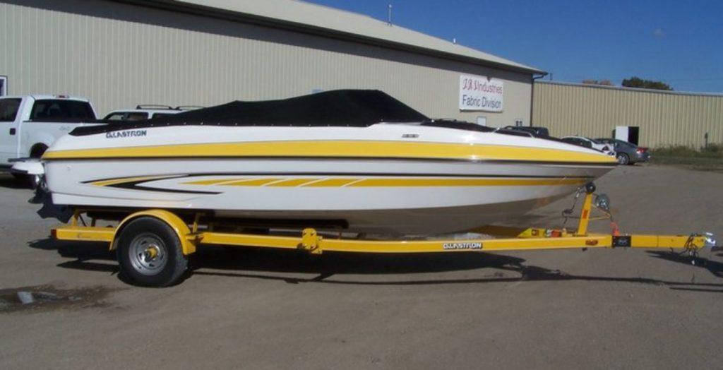 Yellow and white Glastron boat with black cover in front of T.R.S. Industries.