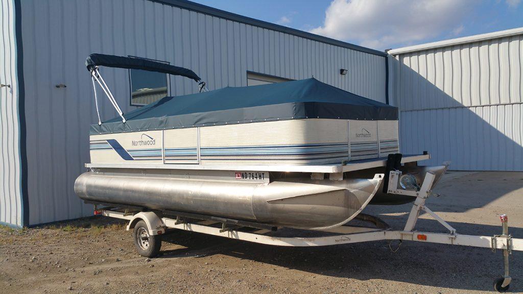 Nothwood pontoon with blue cover in front of T.R.S. Industries.