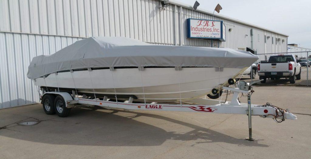 White boat with gray cover in front of T.R.S. Industries.