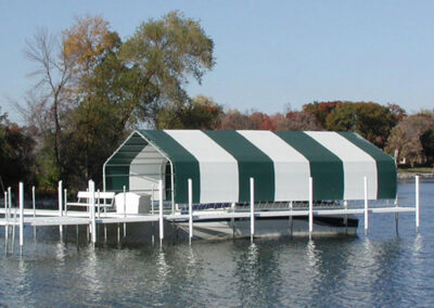 A long white aluminum dock extending into a lake, featuring a boat lift covered by a dark green and white striped canopy canopy frame.