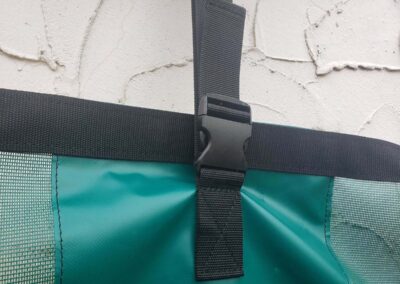 Extreme close-up of a black adjustable plastic buckle and webbing strap sewn onto a teal tarp seam.