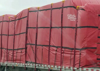 Large flatbed trailer cargo covered in bright red heavy-duty tarps secured with black cargo straps.