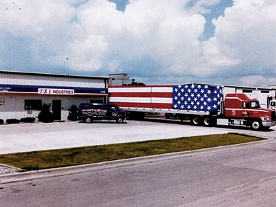 Semi truck with American Flag trailer backed up to building for TRS Industries