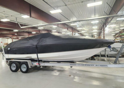 Full side profile shot of a sleek boat completely enclosed inside a storage facility under a tight black ratchet cover.