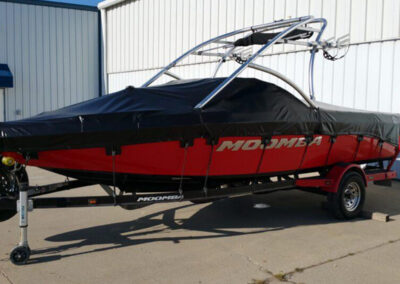Side-angle view of a red and black sport boat on a single-axle trailer, fitted with a black custom trailer-mountable storage cover.