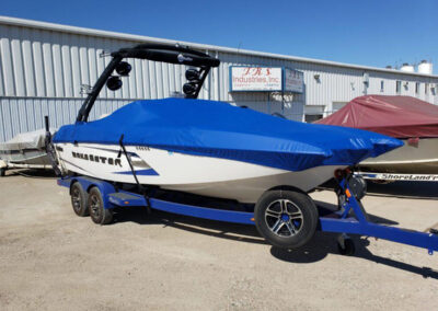 Side angle of a white and blue boat on a trailer secured under a tight-fitting blue custom canvas storage cover.