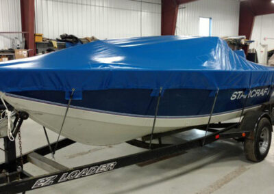 Side-angle view of a white boat on a black trailer, protected under a vibrant royal blue custom trailerable travel cover.