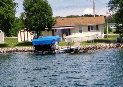 Outdoor view of two separate boat lift stations on a lake, one featuring a royal blue canopy and the other a light tan canopy cover.