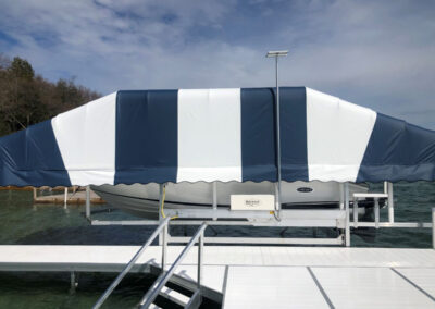 Front-angle view of a blue and white striped boat lift canopy system next to an aluminum modular dock walkway with safety stairs.