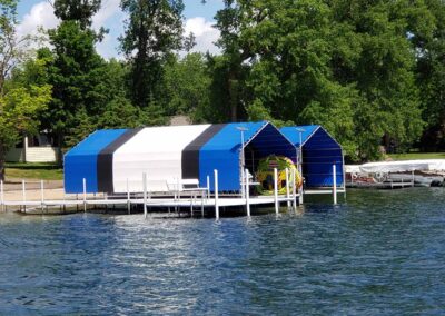 A large double-ended blue and white striped vinyl boat lift canopy sheltering a boat in open water on a clear day.