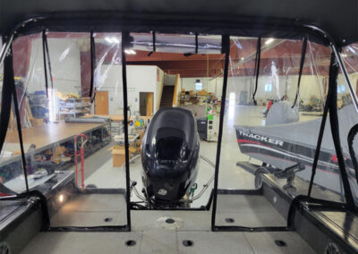 Interior view looking through the clear vinyl windows of a boat bimini top enclosure, showing straps and hardware.