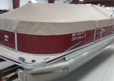 Tan pontoon boat cover with burgundy accent trim fitted over a pontoon boat.