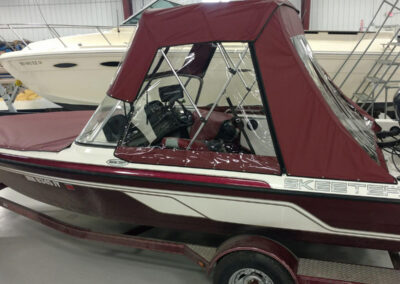 Side view of a burgundy marine canvas bimini top integrated with a clear vinyl front windshield panel.