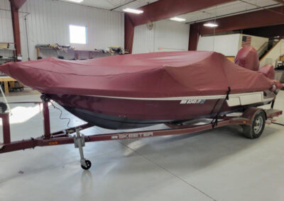 Close-up side view of a trailered boat showing a tightly secured burgundy or dark red marine canvas ratchet cover.