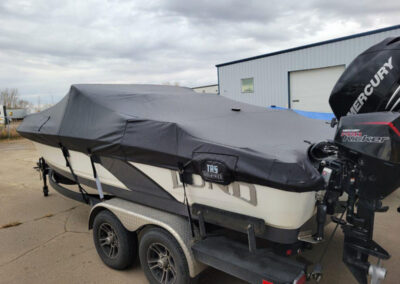 Side-angle perspective of a sport boat with a wakeboard tower securely sealed under a charcoal gray custom ratchet cover.