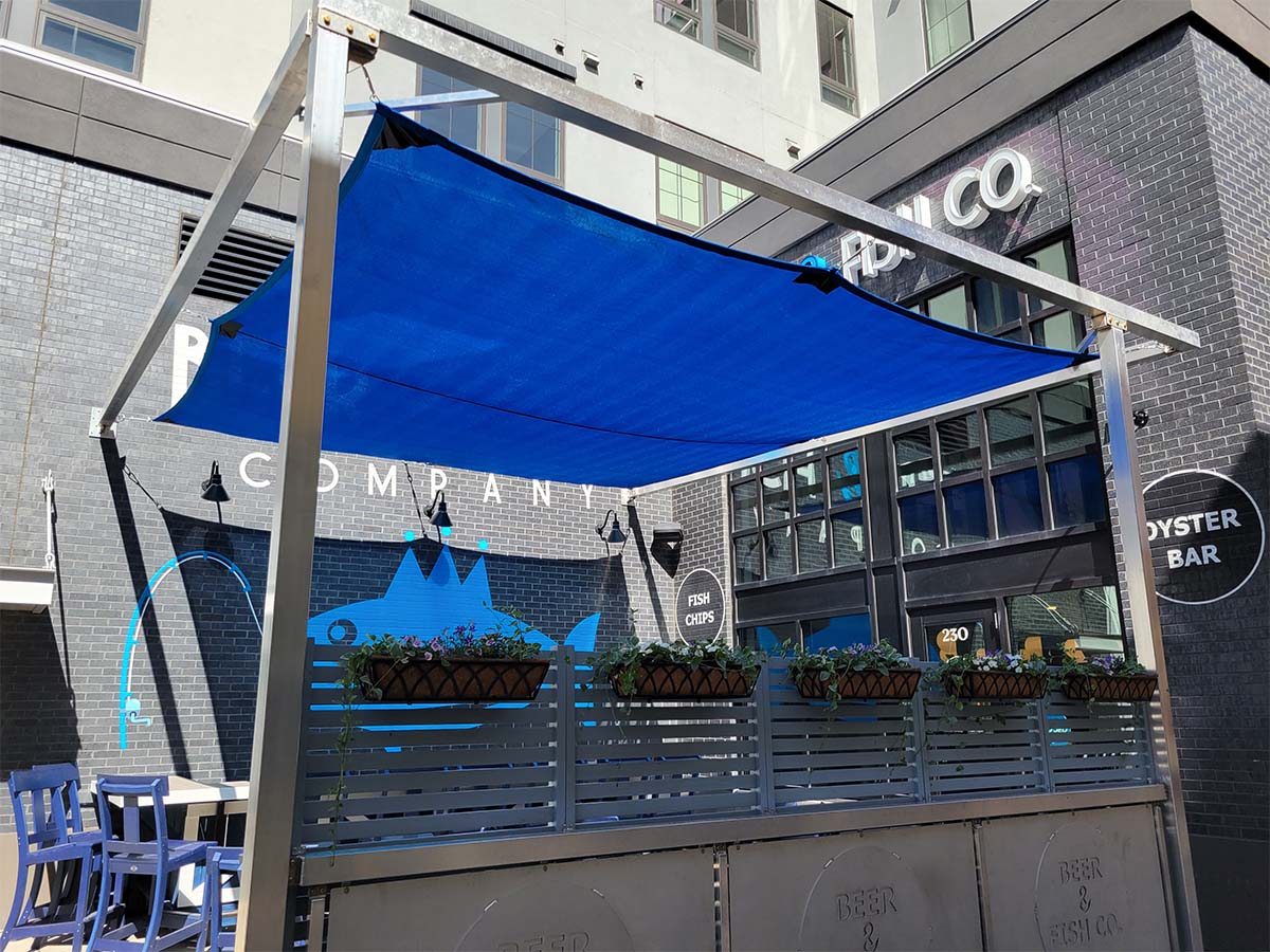 commercial-outdoor-patio-shade-sail A large blue shade sail custom-tensioned above a busy restaurant or bar outdoor patio.