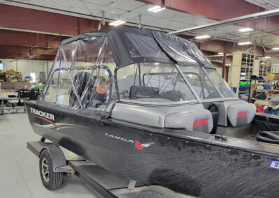 Profile view of a boat featuring a custom-fitted dark gray canvas bimini top and matching clear window side curtains.