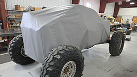 custom-off-road-vehicle-storage-cover An extreme-terrain vehicle completely enveloped in a custom light grey protective cover.