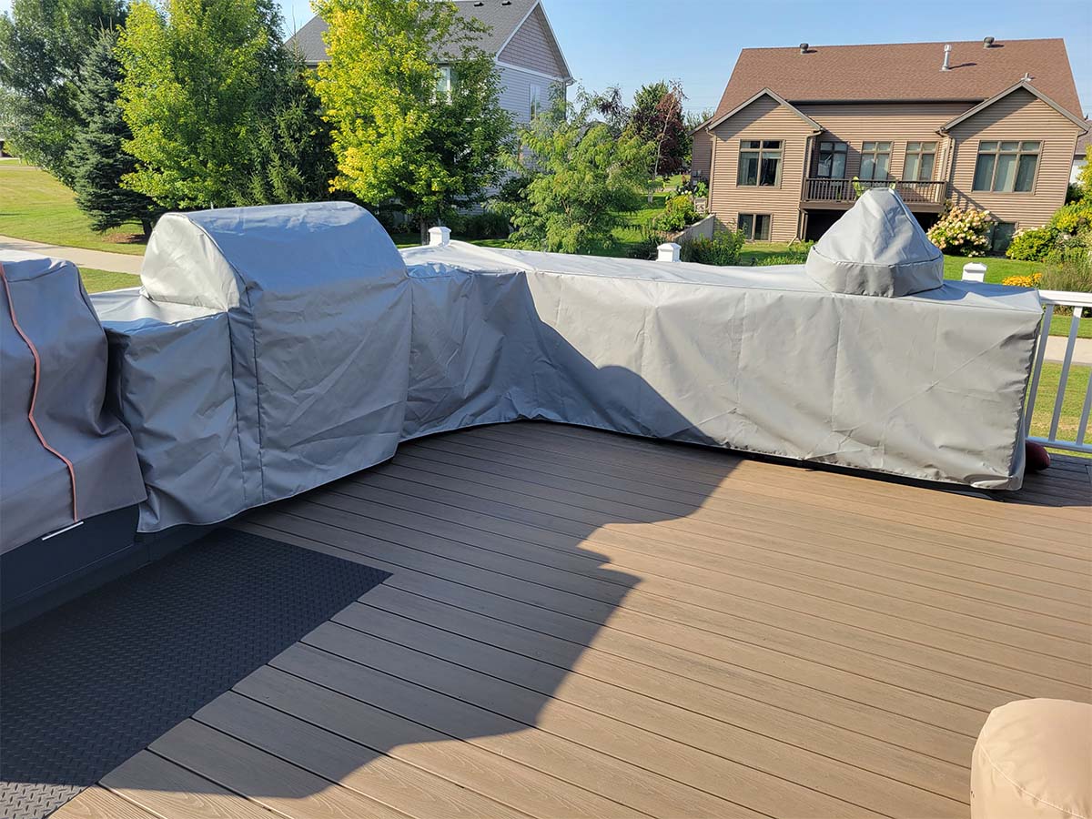 custom-outdoor-kitchen-grill-covers Custom-fitted light grey protective covers protecting a built-in outdoor kitchen with a grill and counter.