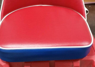 Close-up view of a custom upholstered seat cushion in red vinyl with white piping and a blue side base.