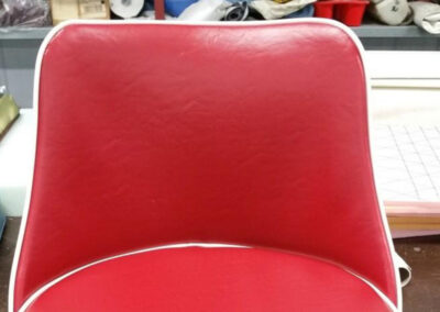 Close-up view of the backrest section of a custom upholstered seat in red vinyl framed with white piping.