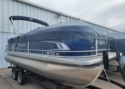 Dark blue fitted boat cover covering a pontoon boat parked outdoors.