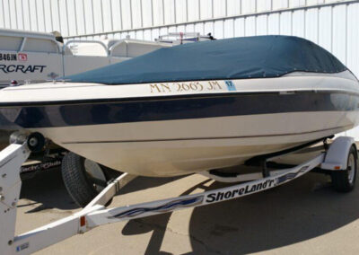 Side view of a white boat on a trailer outdoors, protected by a tight dark blue snap-on cockpit cover.