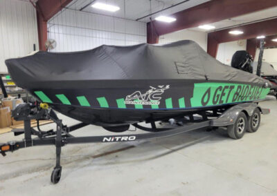 Side view of a sport boat with distinct bright green graphic styling wrapped tightly in a charcoal gray ratchet storage cover.