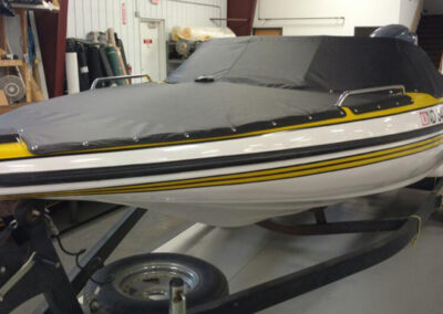 Angled side shot of a classic trailered boat inside a shop facility, secured with a custom dark gray snap-on cockpit enclosure.