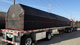 flatbed-semi-truck-lumber-tarp-products A semi-truck flatbed trailer with a tall stack of lumber completely covered by a black lumber tarp.