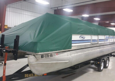 Forest green full coverage pontoon boat cover stored indoors on a trailer.
