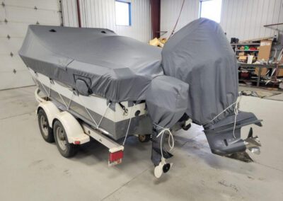 Rear-angle shot of a trailered boat wrapped tightly under a comprehensive gray canvas storage cover with full transom coverage.