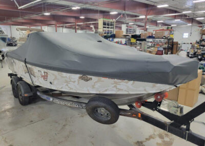 Profile angle of a white fiberglass boat on a single-axle roller trailer protected by a tightly fitted gray ratchet cover.