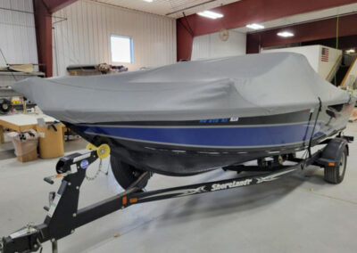 Side view of a blue-hulled sport boat on a trailer outfitted with a custom-molded gray ratchet tie-down cover.