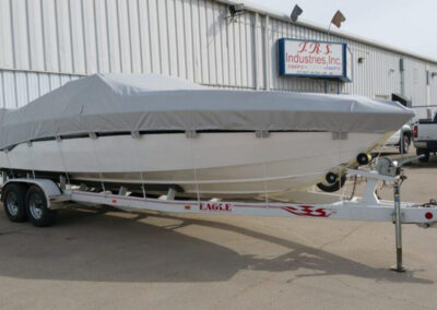 Profile shot of a white boat on a heavy-duty aluminum trailer, fully enclosed under a tightly fitted gray custom travel cover.