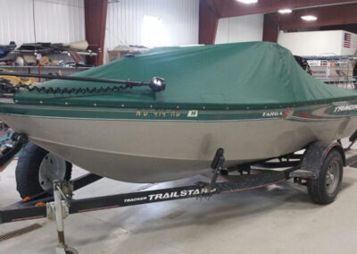 Side profile shot of a green-accented boat on a trailer indoors, utilizing a tight-fitting green snap-on cockpit cover.