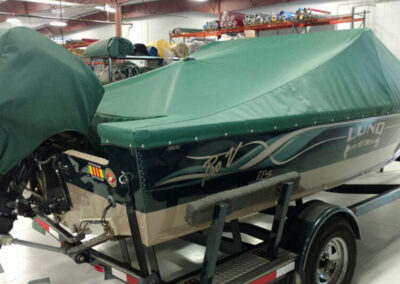 Three-quarter rear view of a dark green boat hull featuring a matching green snap-on cockpit cover and full outboard motor shroud.
