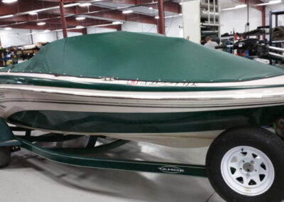 Side-profile view of a sport boat on a single-axle trailer utilizing a forest green snap-on bow and cockpit cover.