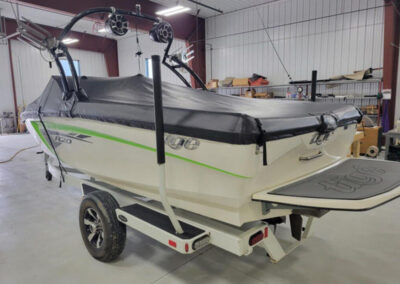 Side-view image of a white boat on a trailer featuring a custom light gray canvas travel and storage cover.