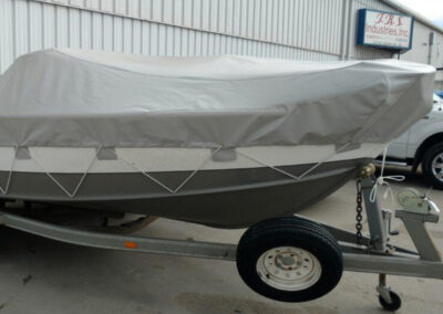 Detailed side view of a boat secured under a tight, form-fitting light gray protective cover fastened with hull hooks.