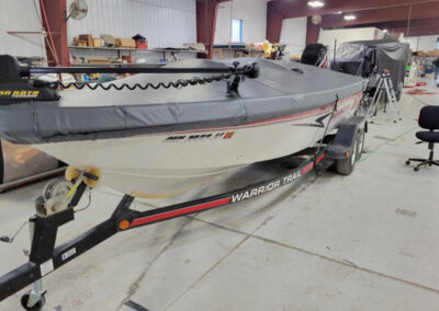 Side profile of a boat on a trailer equipped with a form-fitting light gray canvas cover utilizing a ratchet hem line.