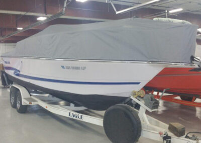 Side view of a white boat on a trailer inside a workshop, featuring a clean light gray snap-on cockpit enclosure cover.