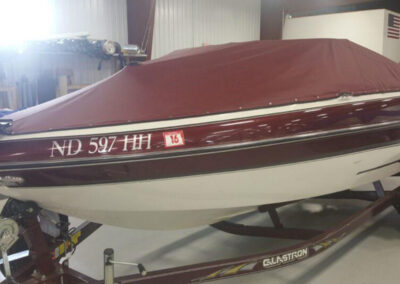 Profile view of a sleek red-striped boat on a trailer fitted with a matching deep maroon snap-on cover set.
