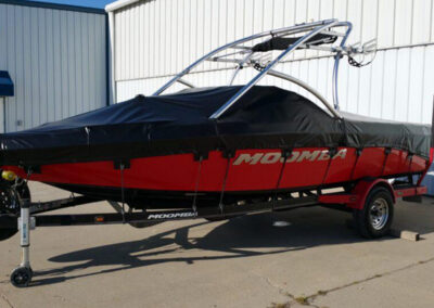 Side profile of a sport boat on a trailer featuring a fitted, two-tone black and red custom travel cover.