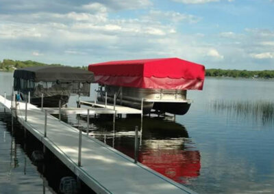 A vivid red boat lift canopy station positioned at the far end of a long white sectional residential dock layout on a calm lake.