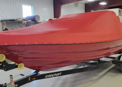 Front-angle view of a boat on a trailer fully enclosed from bow to stern under a striking red custom snap-on cover.