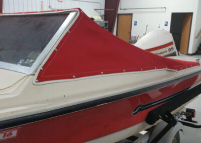 Side-angle view of a white boat with a large windshield frame wrapped tightly in a red custom snap-on cockpit cover.