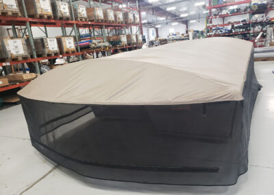 Indoor display model of a tan boat lift canopy top integrated with a full-length black protective mesh netting screen.