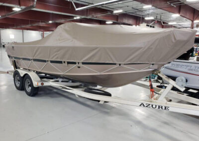 Side-angle view of a white boat on a trailer outfitted with a custom tan marine canvas cover utilizing integrated lashing hooks.