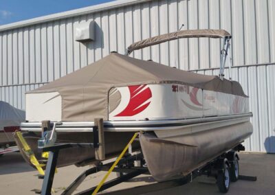 Tan custom mooring cover with red graphics fitted on a pontoon boat on a trailer.